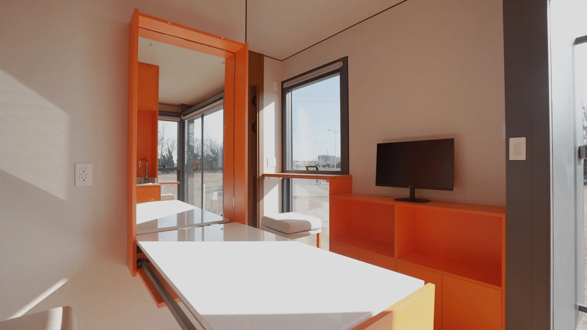 Nestron modular home interior with orange cabinetry, wall-mounted TV, and large windows