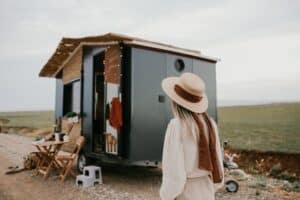 A woman with a hat standing in front of a tiny home.