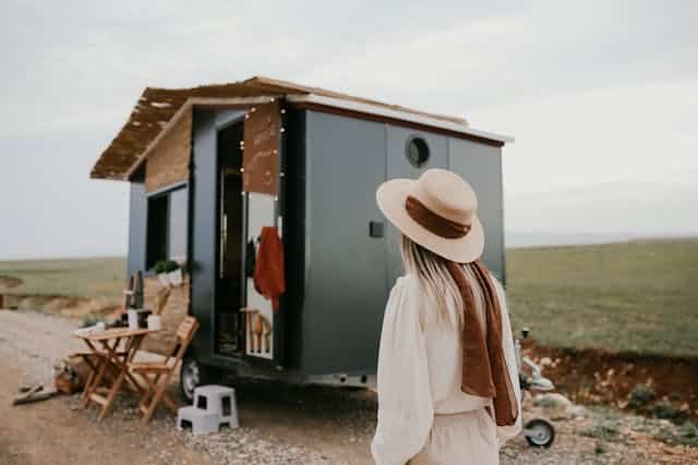 A woman with a hat standing in front of a tiny home.