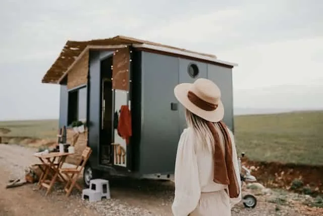 A woman with a hat standing in front of a tiny home.