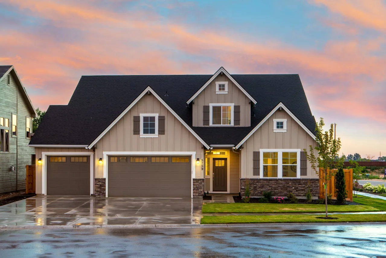 Exterior view of a two-story suburban home with a three-car garage, landscaped yard, and illuminated windows at sunset