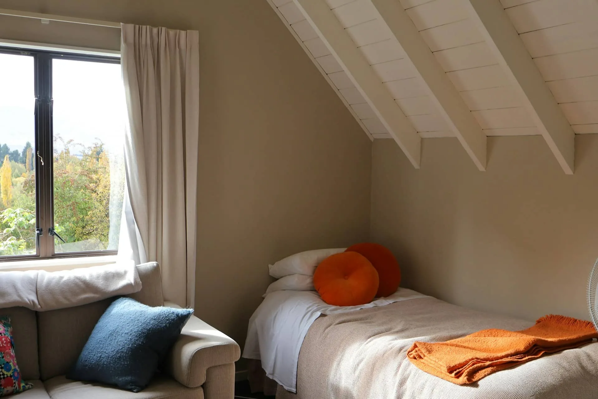 Cozy bedroom interior with sloped ceiling, neutral walls, curtains, and natural light