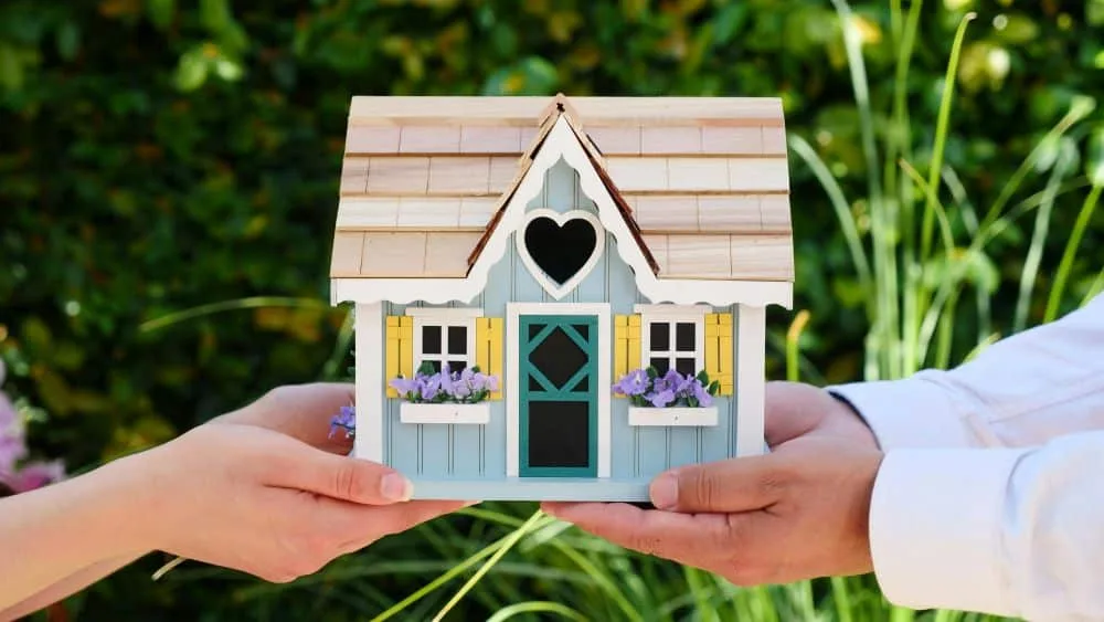 Small model house held in hands, representing backyard ADU investment or rental income