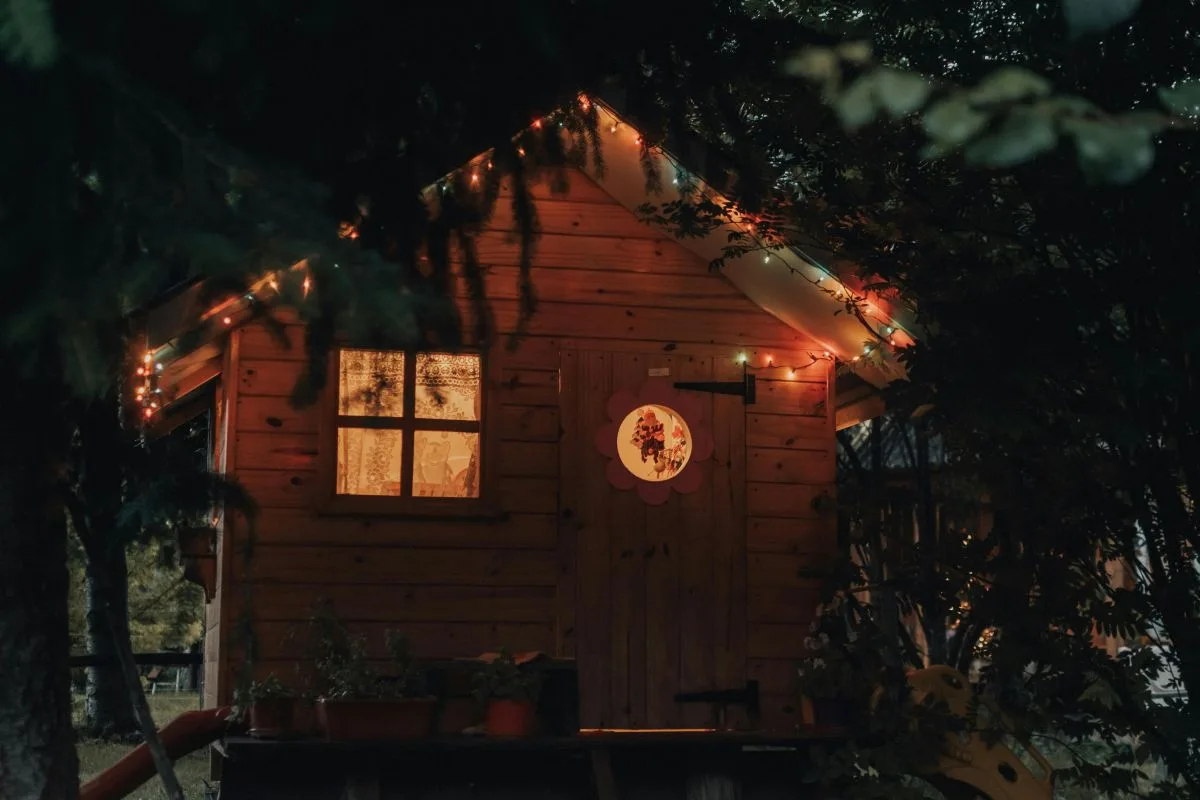 Exterior night view of a small home with warm interior lighting and surrounding trees