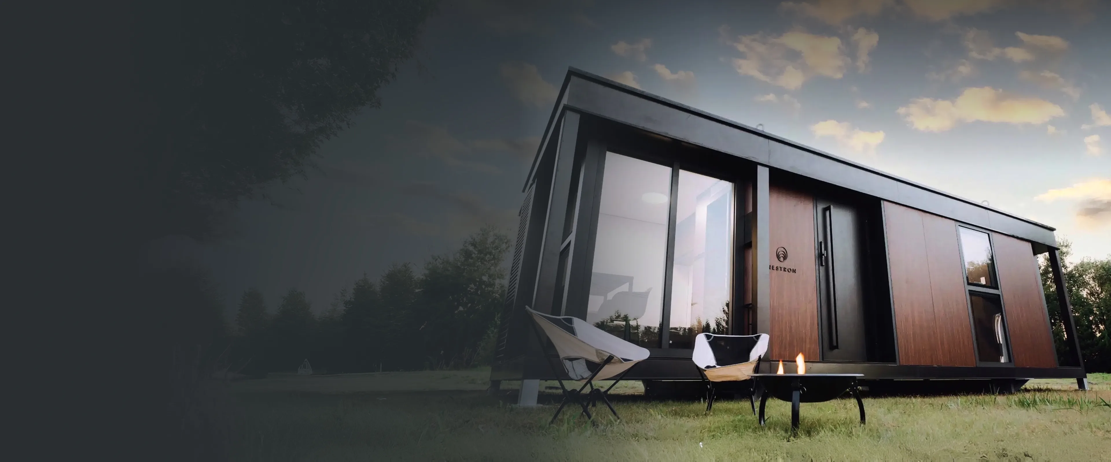 Modern modular home exterior at dusk with floor-to-ceiling windows and outdoor seating