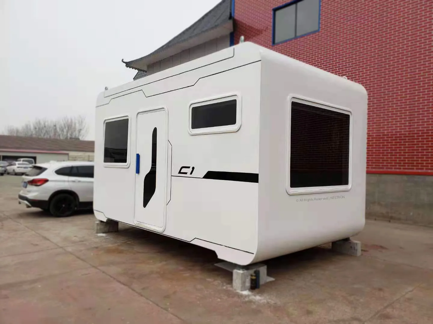 Rear exterior view of the Nestron Cube One with a white facade, dark trim, small windows, and a rooftop vent