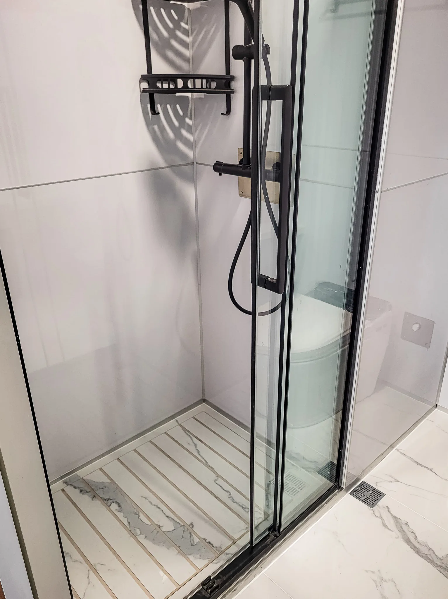 Close-up rendering of the Nestron Cube One glass shower enclosure with black fixtures and white tiled walls