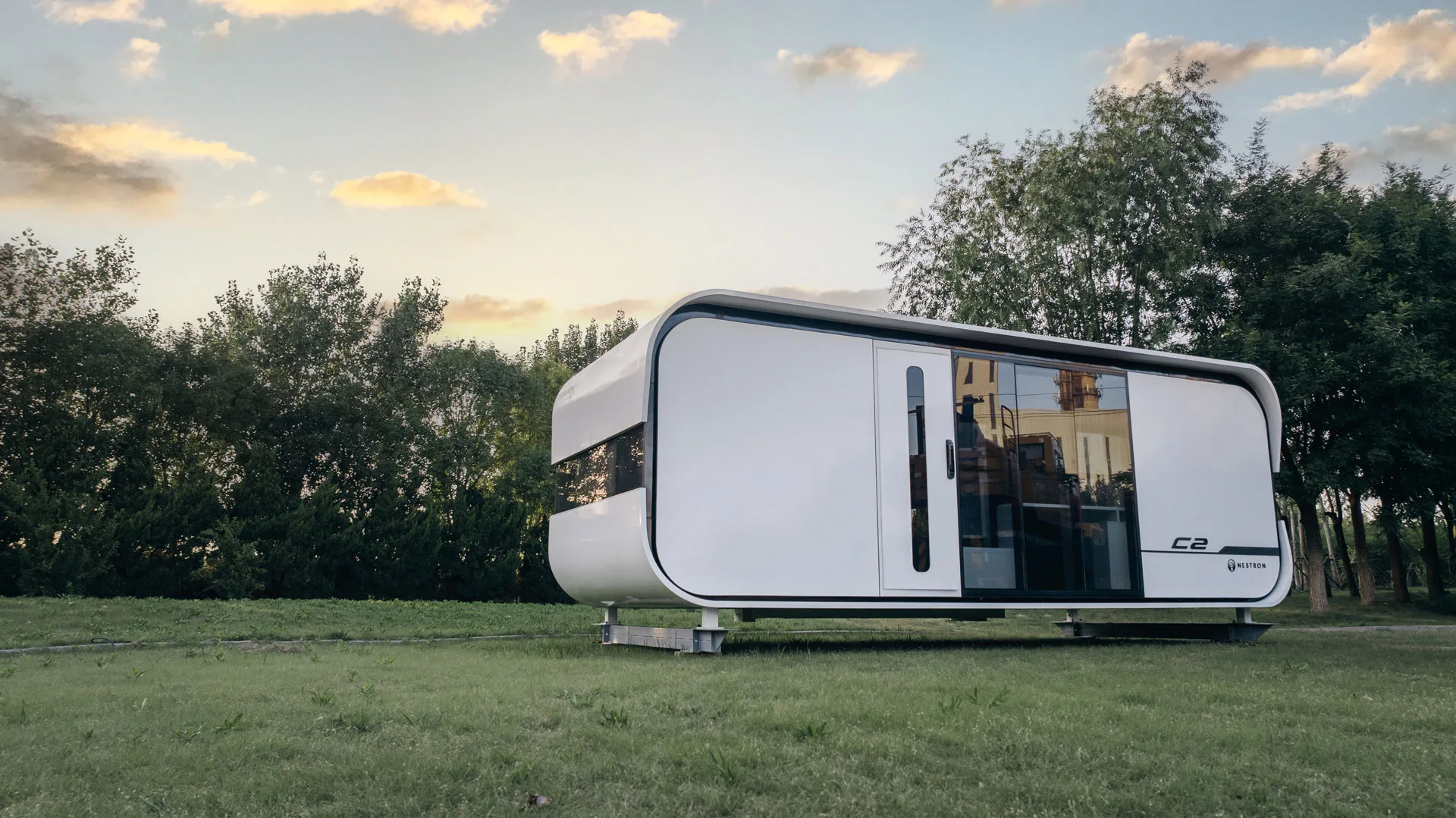 Exterior rendering of the Nestron Cube Two on a grassy landscape with trees and a cloudy sky