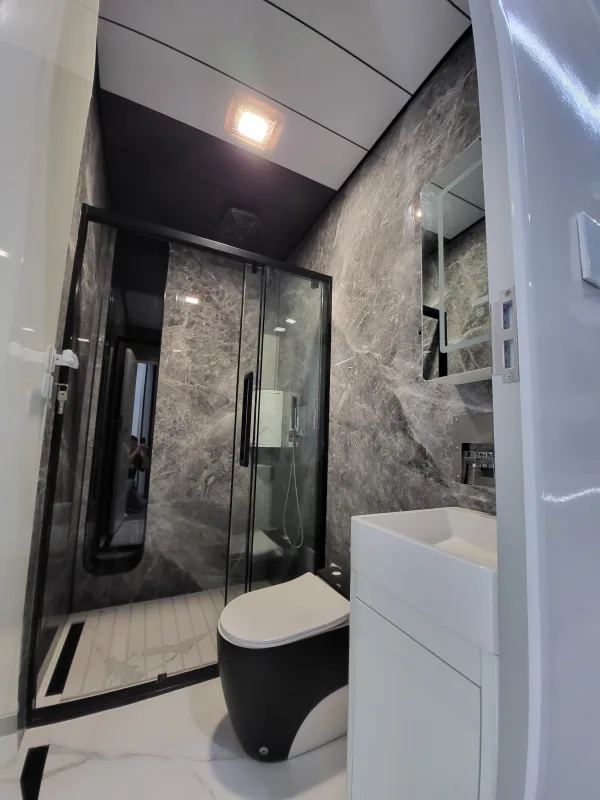 Nestron Cube Two X bathroom rendering with a glass shower enclosure, white vanity, toilet, and stone-look wall panels