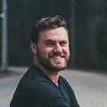 Portrait of a smiling man with dark hair and a beard wearing a black shirt
