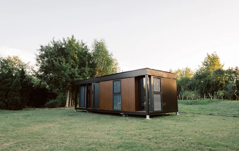 Exterior view of a modern modular home with wood siding, large windows, and a grassy natural setting