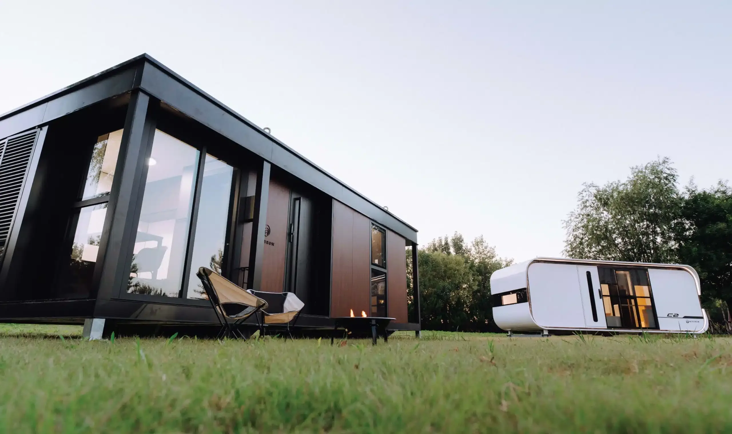 Exterior view of a modern modular home with dark siding, large windows, and a grassy foreground