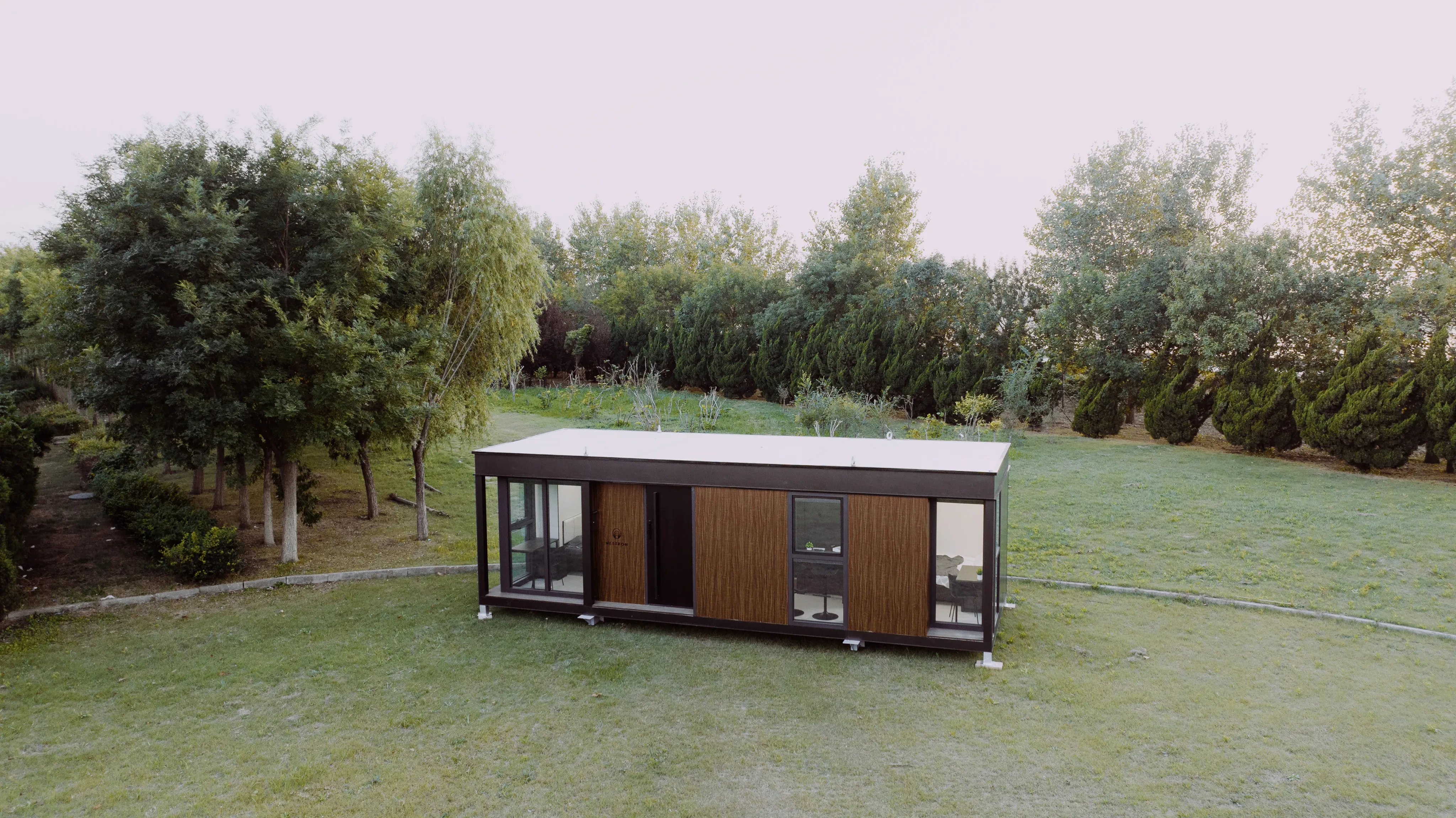 Exterior view of a long wood-sided modular home surrounded by grass and trees