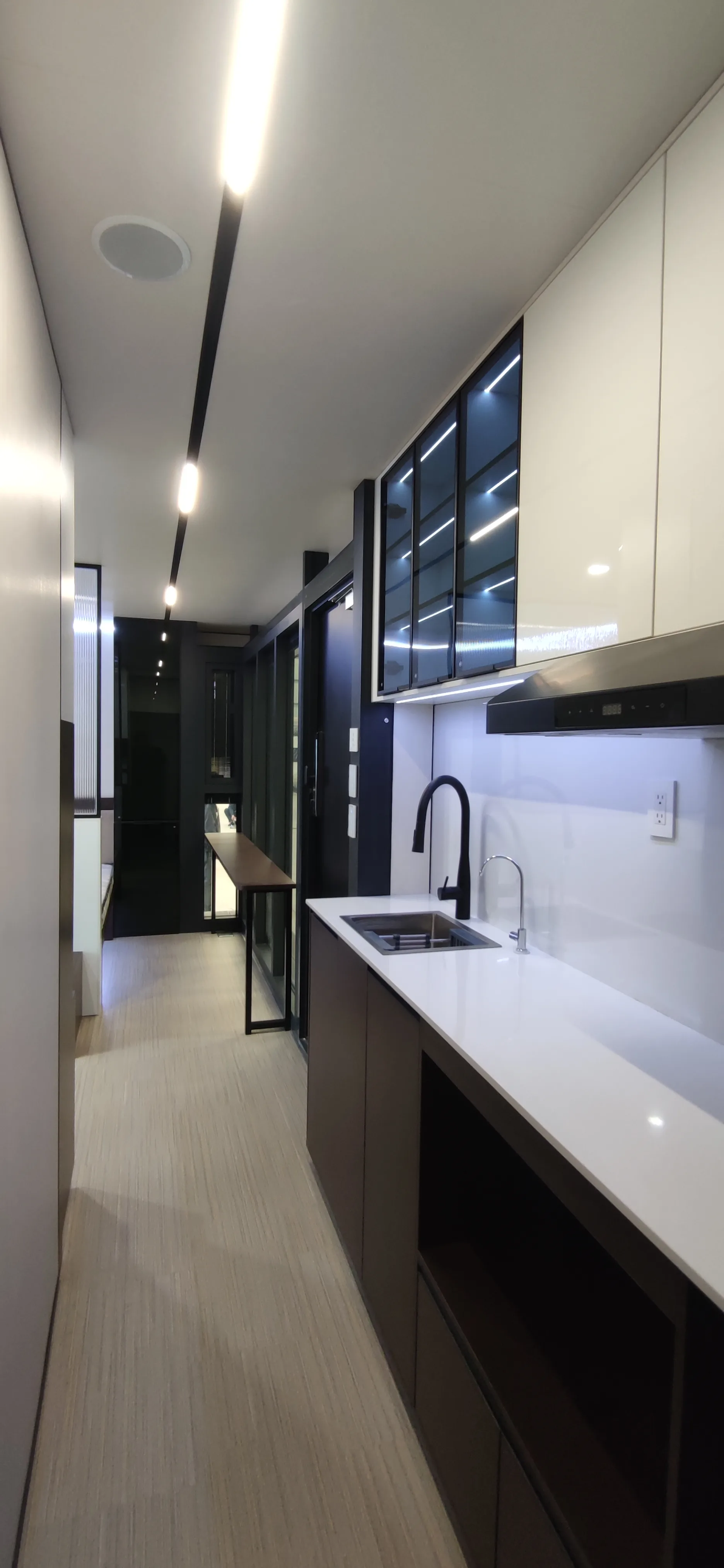 Nestron Legend One kitchen interior with a stainless sink, black faucet, range hood, and glass-front upper cabinets