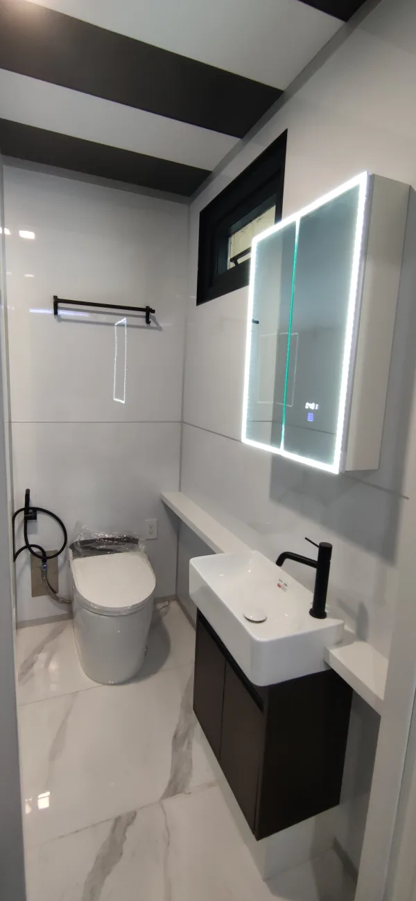 Nestron Legend One bathroom rendering with a white vanity, toilet, illuminated mirror, and black fixtures