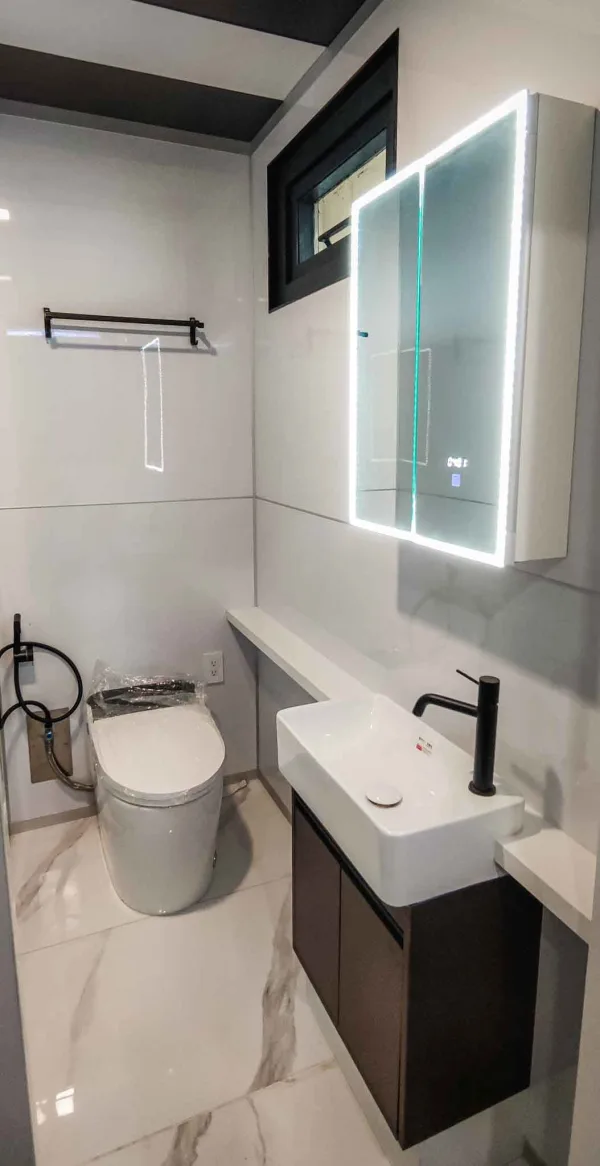 Nestron Legend One bathroom rendering with a white vanity, toilet, illuminated mirror, and tiled walls