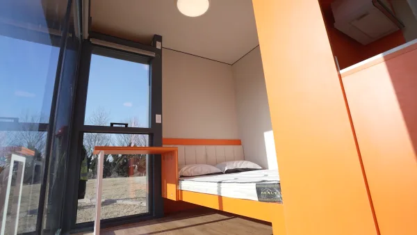 Nestron Legend Two bedroom rendering with a bed, large window, and orange interior accents