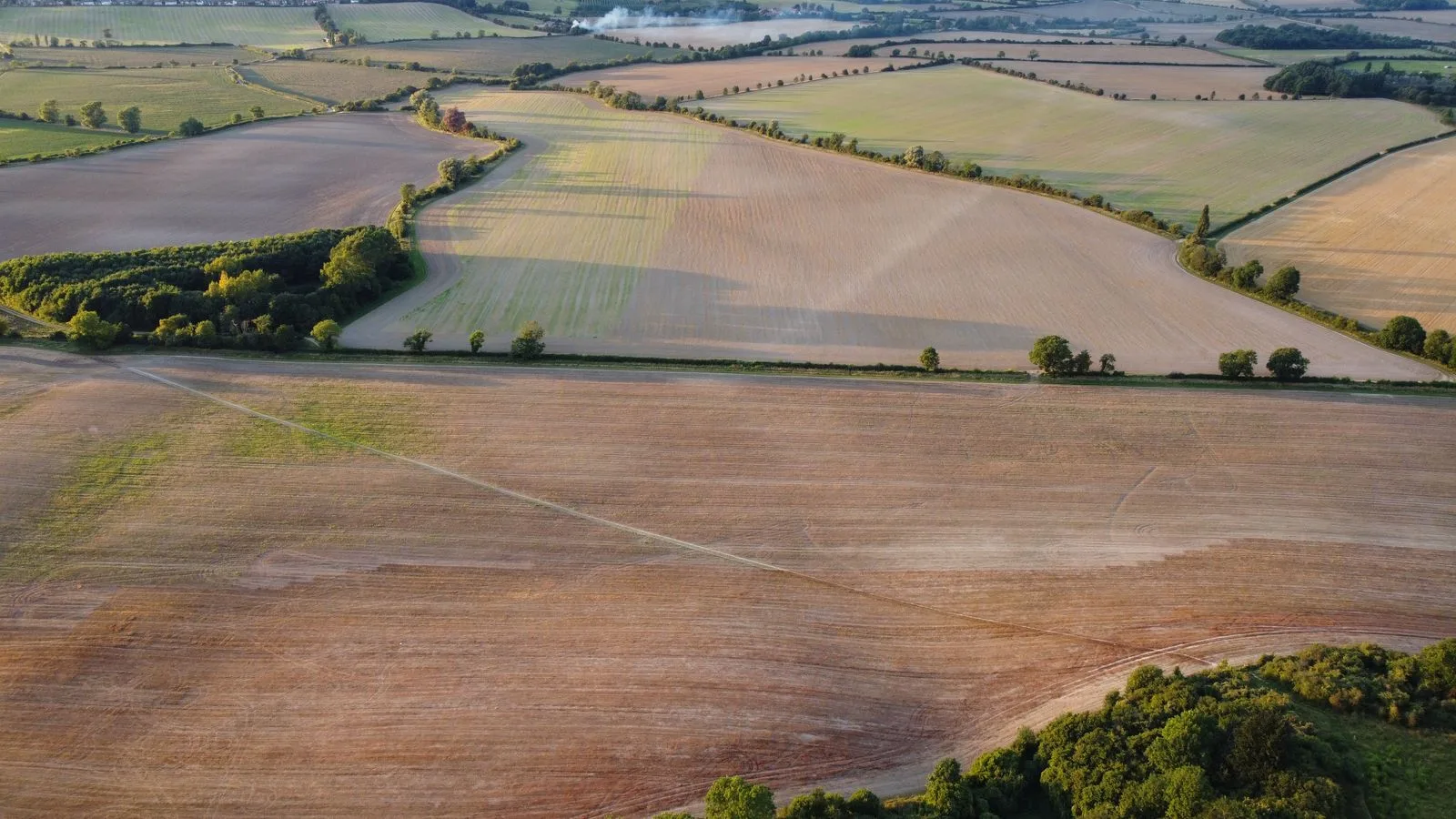 Aerial view of undeveloped rural land with open fields, tree lines, and farmland plots