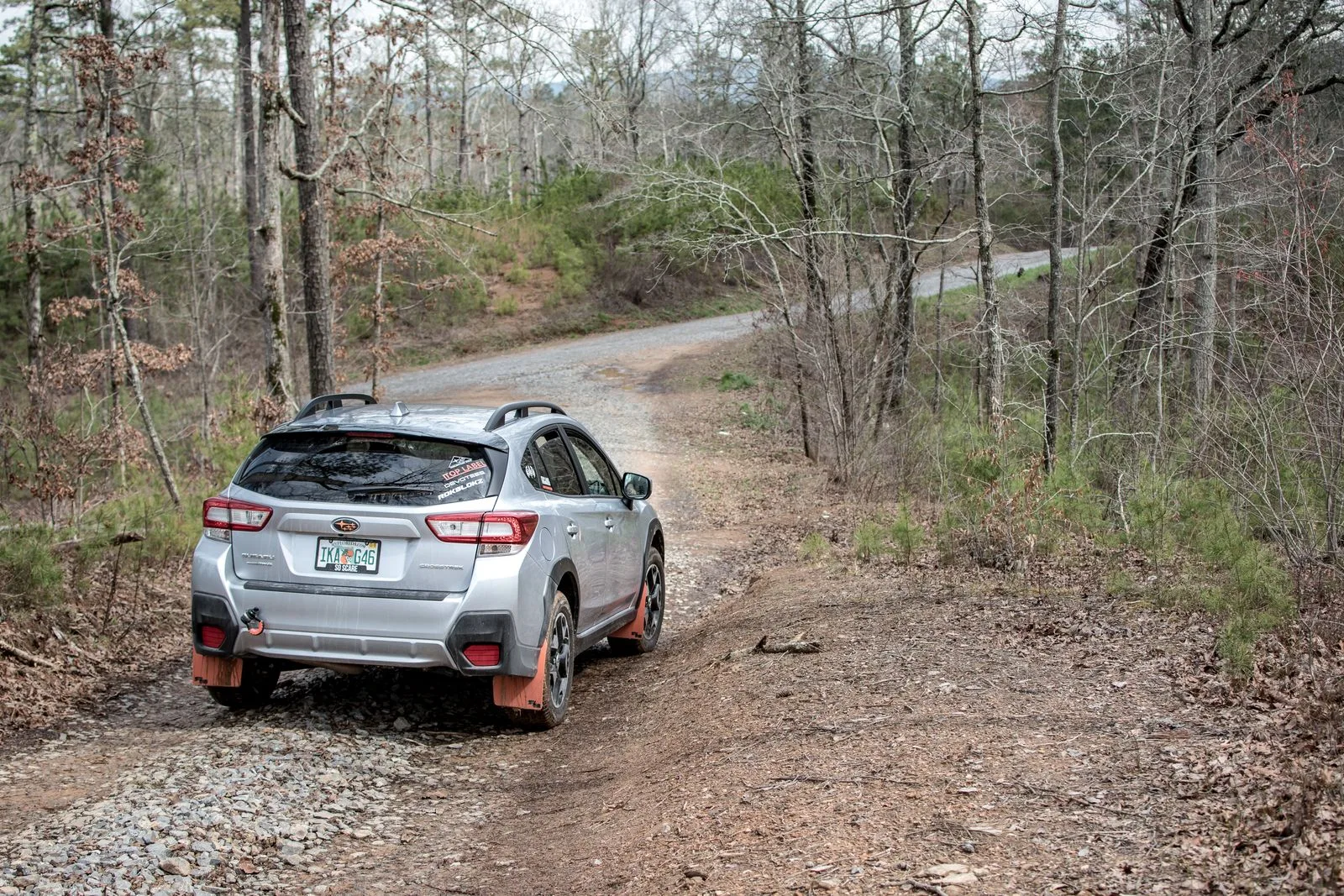 Silver SUV driving along a rough gravel road through a wooded rural area