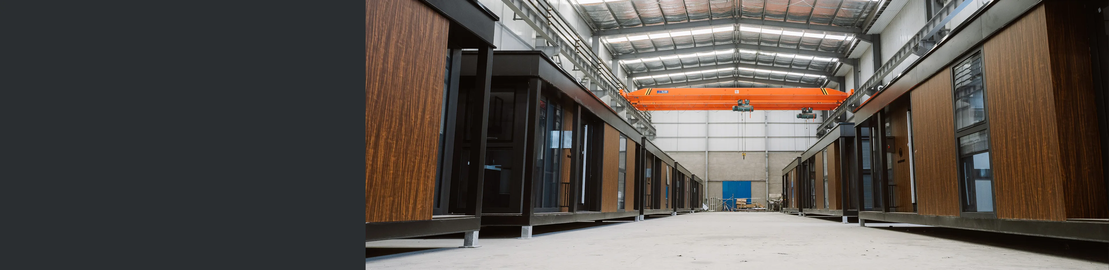 Modular home units lined up inside a production facility with wood siding and large glass doors