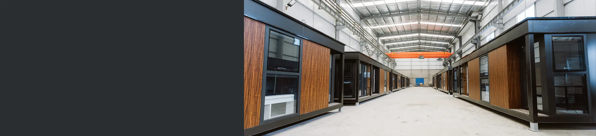 Exterior view of a modular home unit with wood siding and large windows inside a production facility