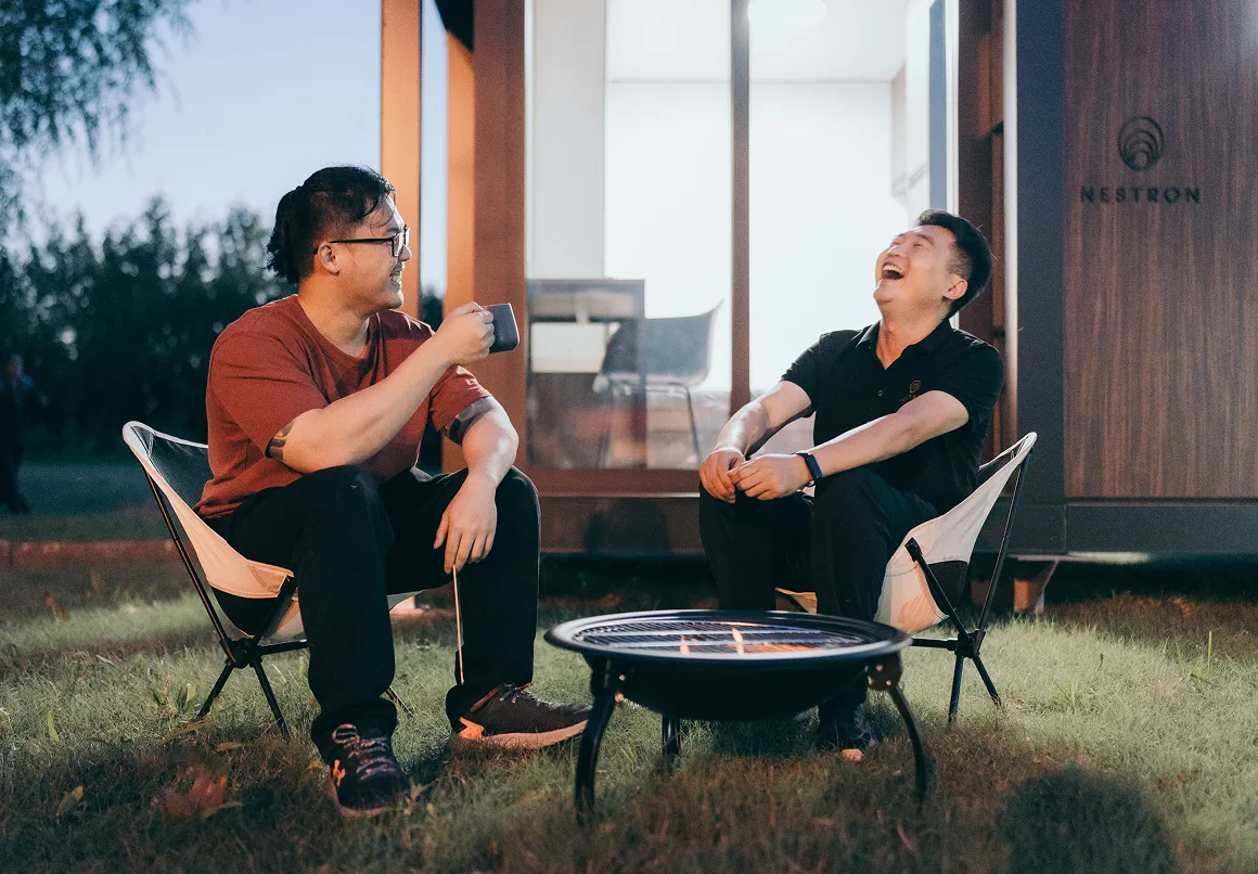 Two people seated outside a modern modular home having a conversation