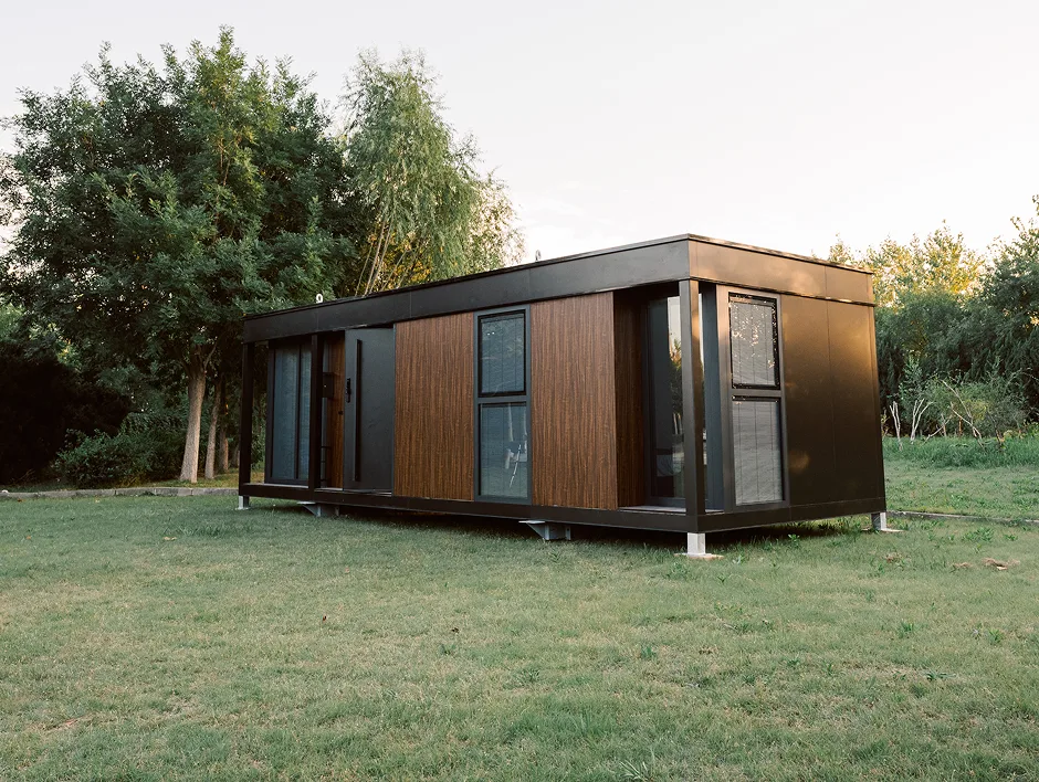 Exterior view of a modern modular home with wood siding, dark trim, and a grassy yard