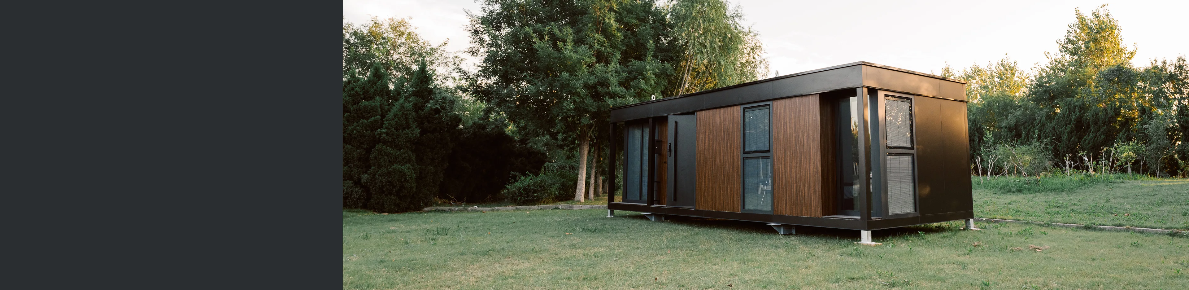 Exterior view of a modern modular home with wood siding, large glass doors, and a grassy yard