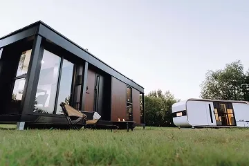 Exterior view of a modern modular home with dark siding, wood accents, and a grassy foreground