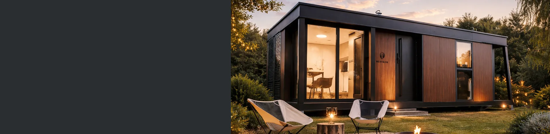 Exterior view of a modern modular home at dusk with large glass windows, warm interior lighting, and outdoor lounge chairs