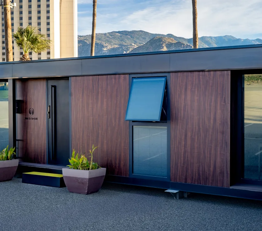 Exterior view of a Nestron modular home with wood siding, entry door, and mountain backdrop