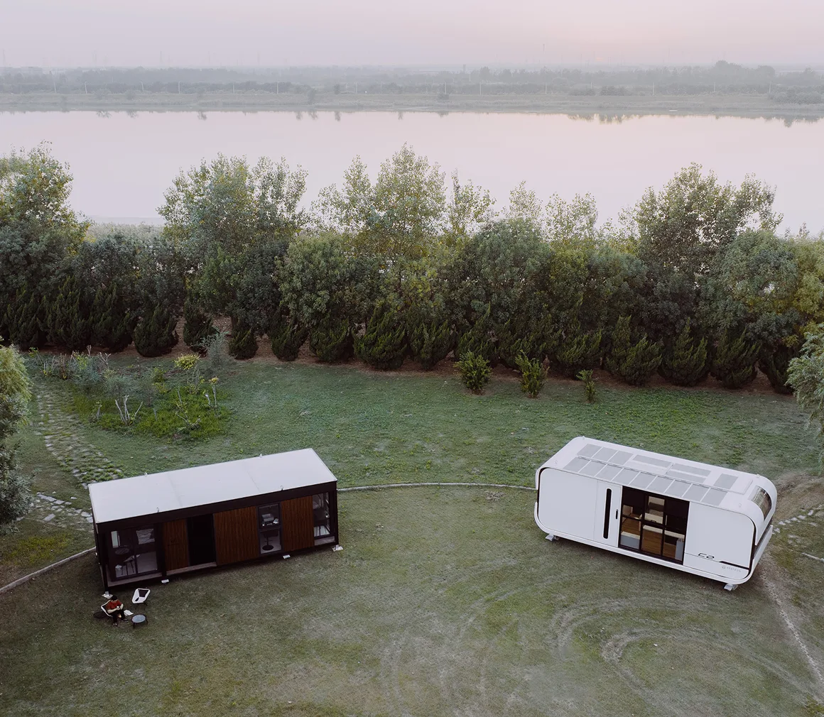 Elevated view of two modular homes positioned in a large grassy clearing surrounded by trees