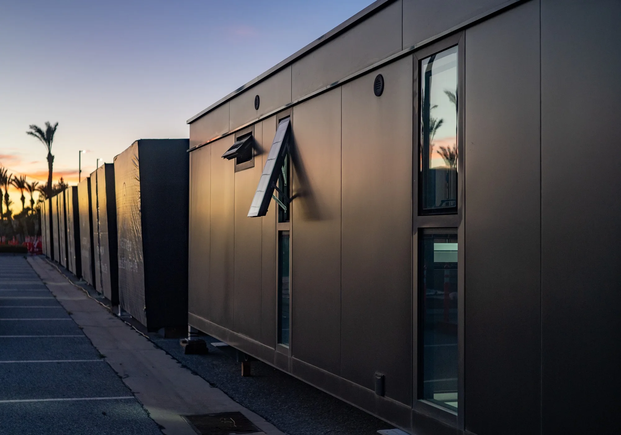 Nestron modular homes with dark paneling lined up outdoors at sunset
