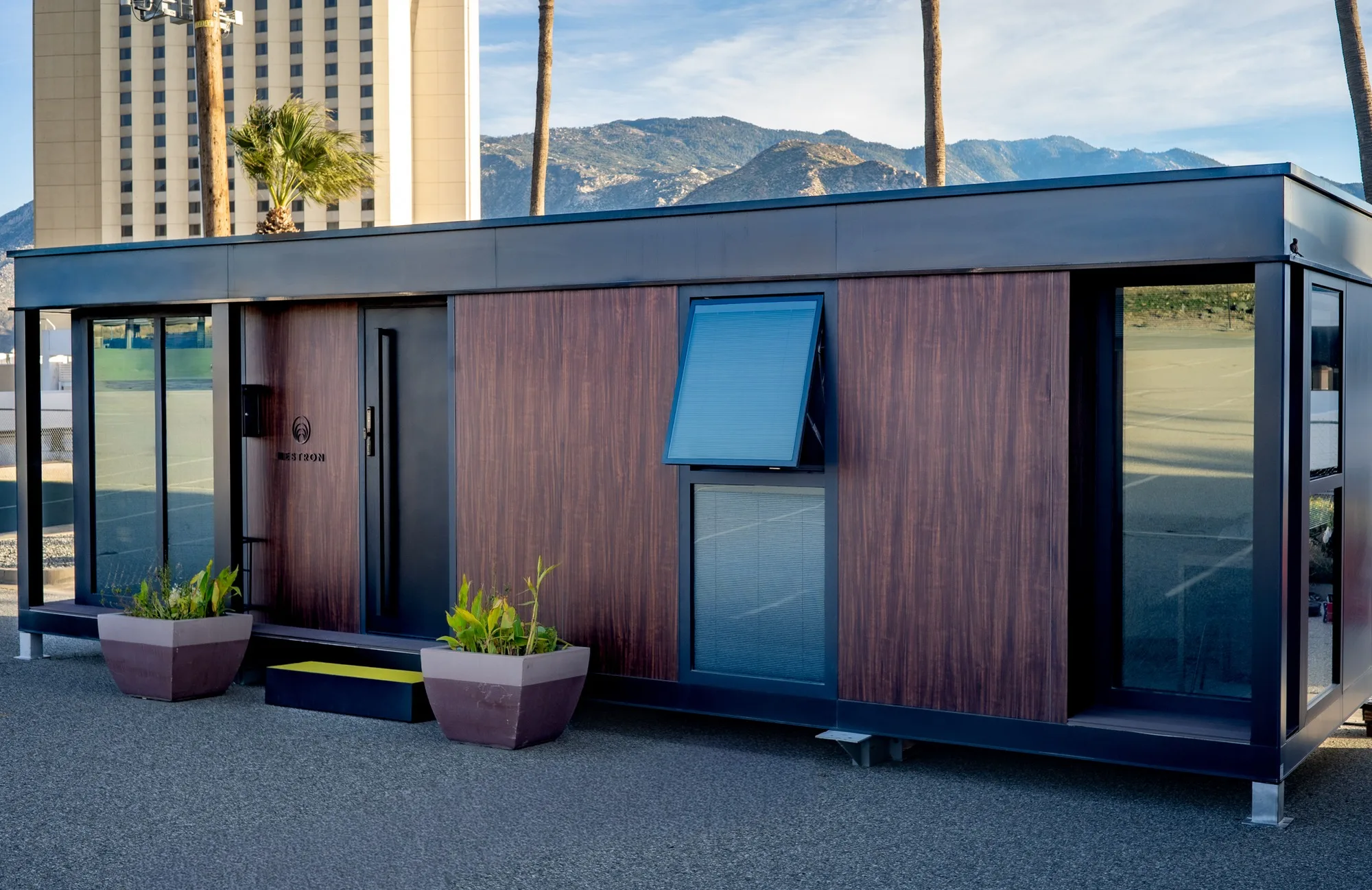 Angled exterior view of a Nestron modular home with wood siding, dark trim, and a blue awning window