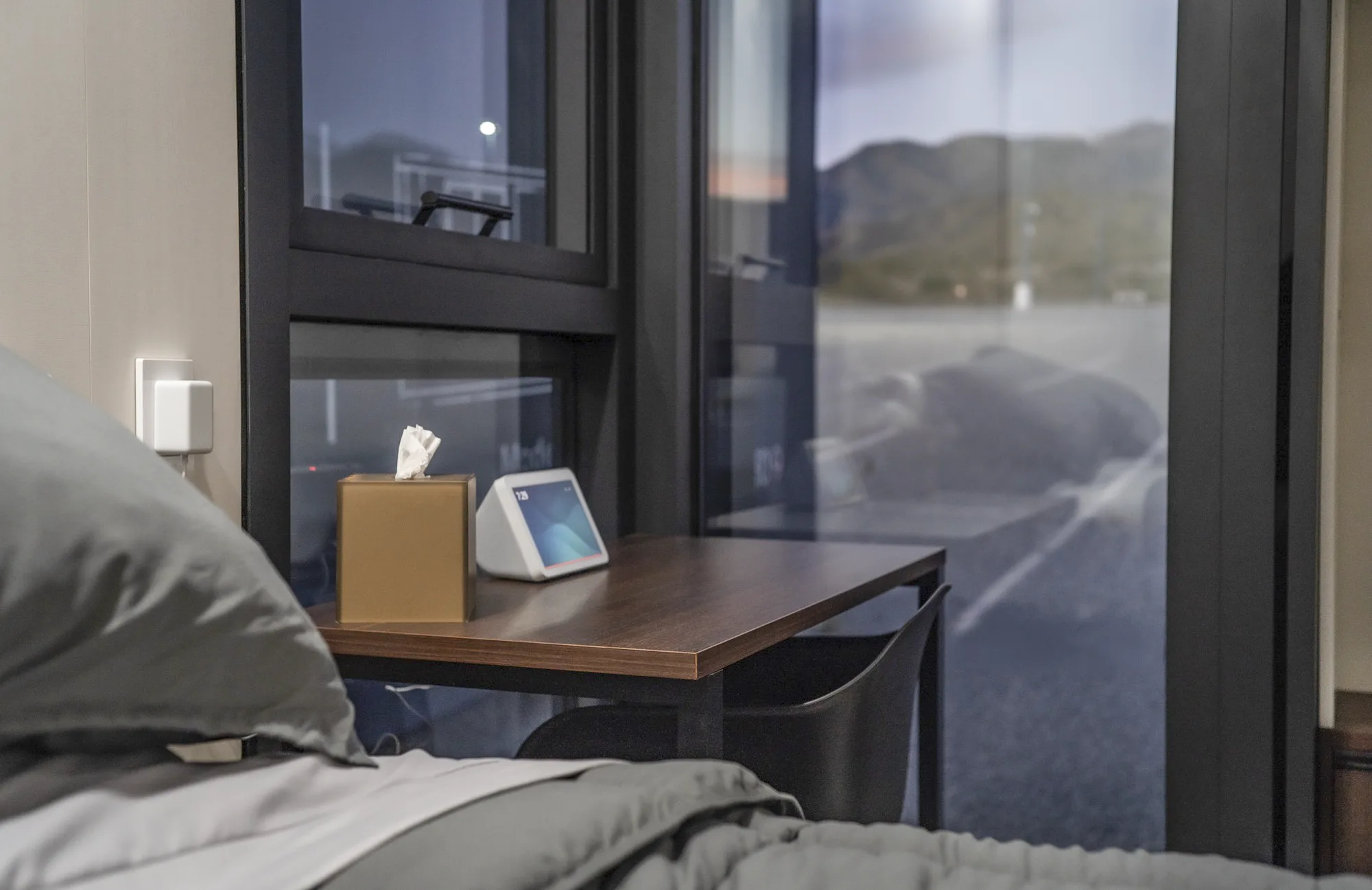 Nestron modular home bedroom nightstand with smart device and window view at dusk