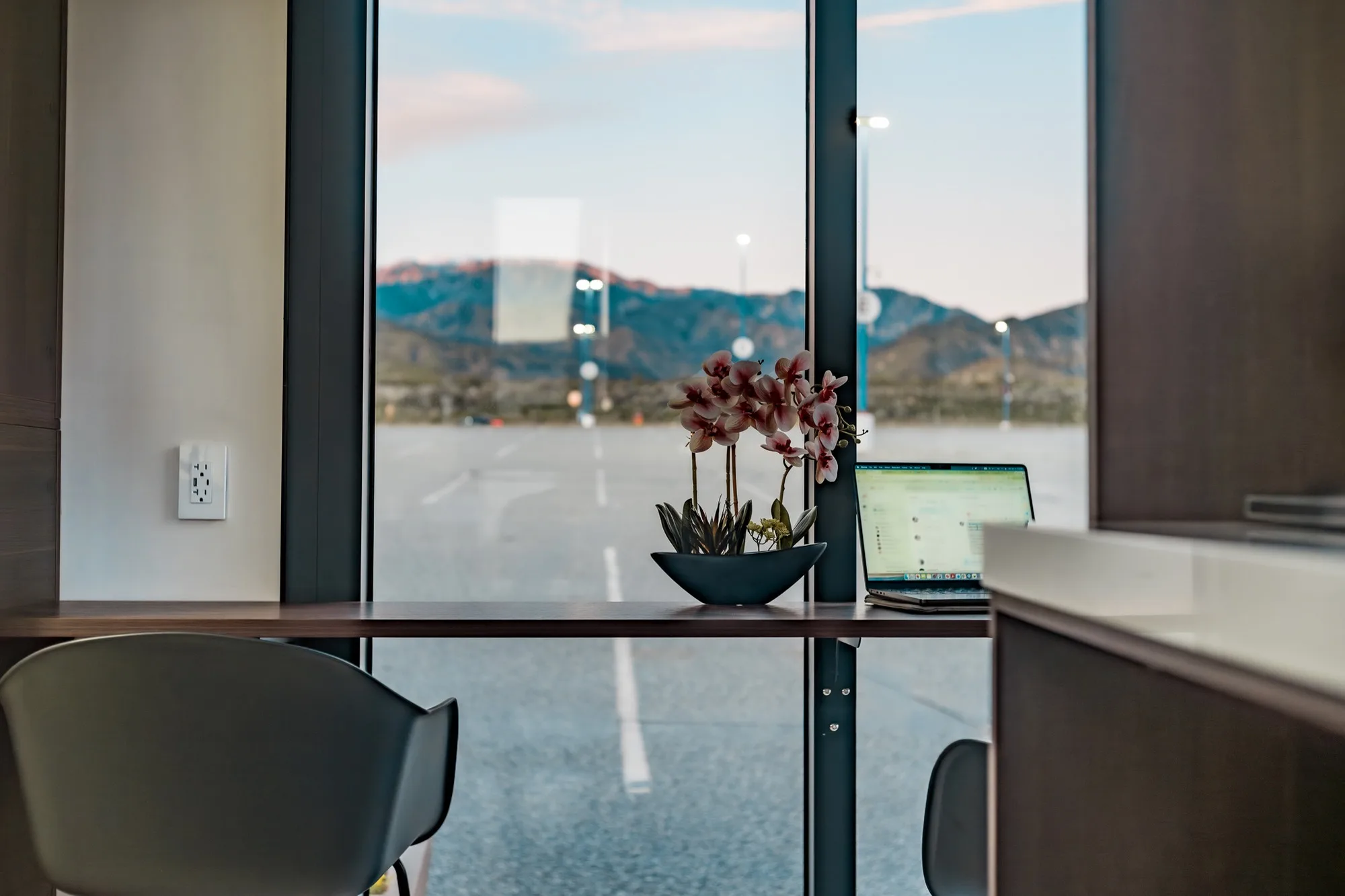 Nestron modular home desk by window with laptop, orchid plant, and highway view, atmospheric feature