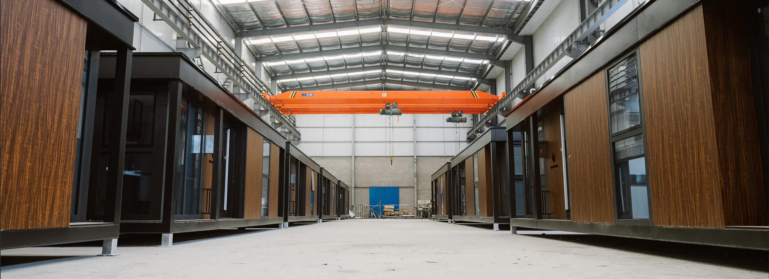 Modular home units lined up inside a factory with dark framing, wood siding, and large glass doors